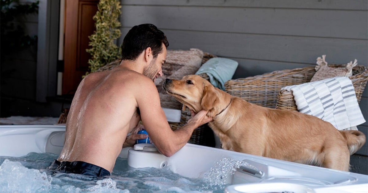 A man in a hot tub in Utah enjoys relaxation as he interacts with a golden retriever, gently touching the dog's face while nearby hot tub accessories enhance the cozy moment.