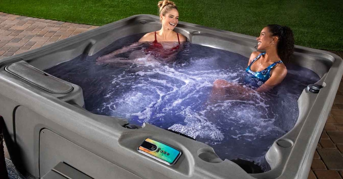 Two people are smiling and chatting in a bubbling hot tub on the patio, enjoying year-round relaxation.