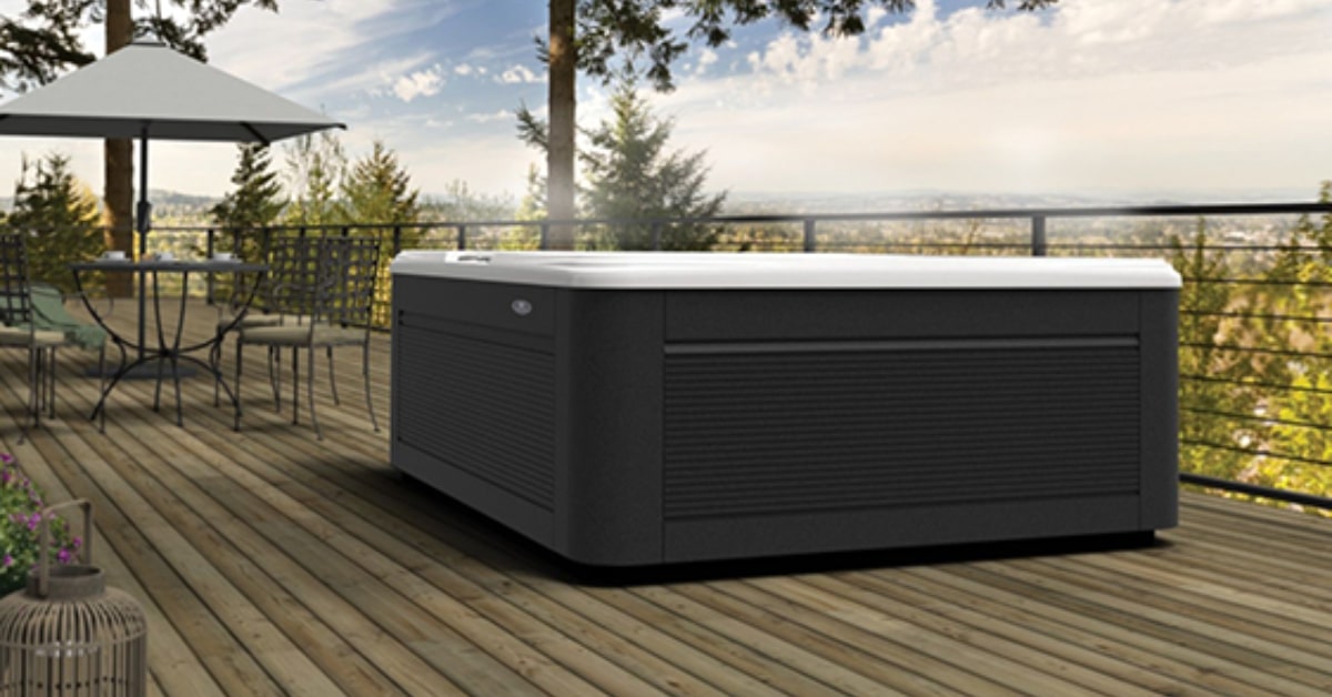 A hot tub from one of Utah's premier spas installations sits on a wooden deck with a patio table and chairs nearby, surrounded by trees and a view of the horizon under a partly cloudy sky.