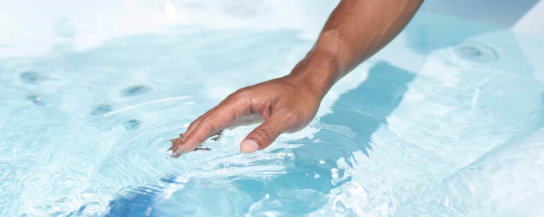 A person’s hand reaching into clear, rippling water.